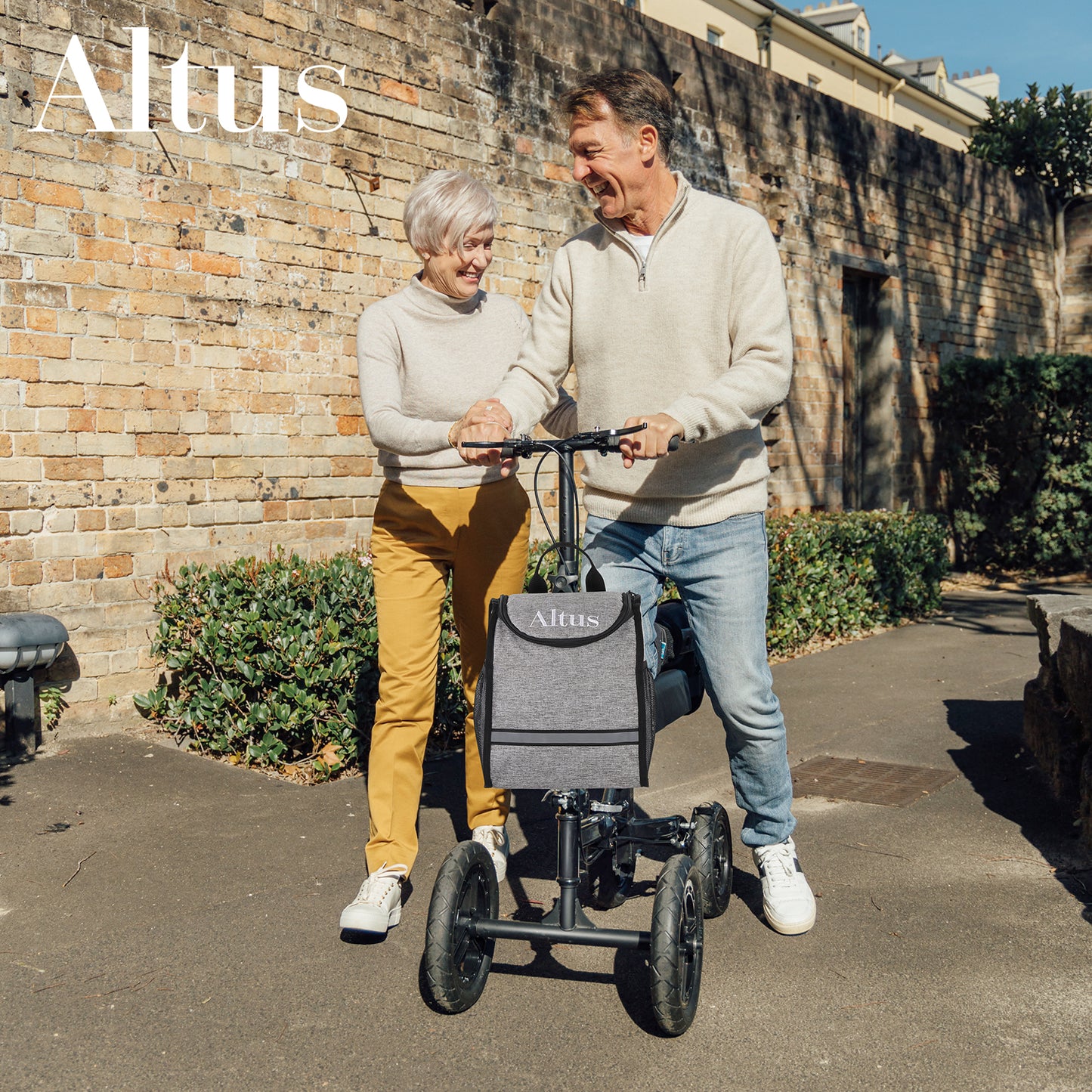 Man and woman with a mobility scooter, walking outdoors near a brick wall.