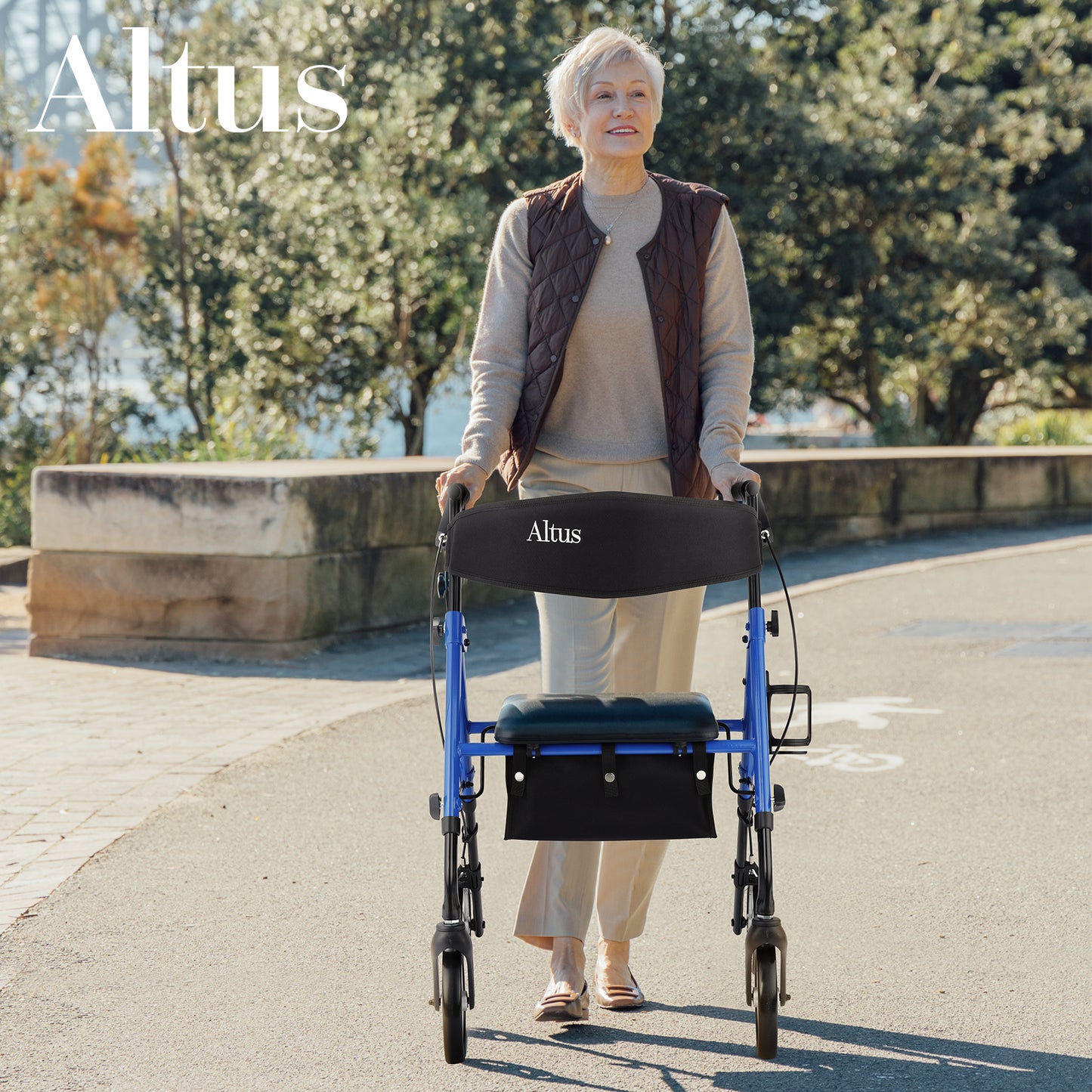 An elderly woman is walking outdoors using an Altus walker with a seat. The walker features a blue frame, a black seat, and a storage bag, blending seamlessly with the natural environment.