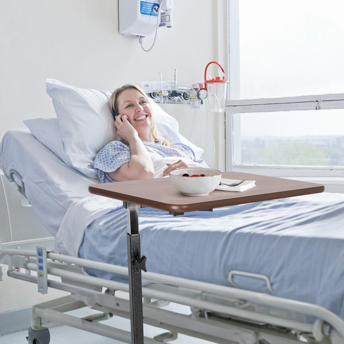 Patient using the Altus Adjustable Overbed Table in a hospital bed, with a walnut laminate tabletop holding a bowl and phone, highlighting the table's convenience and functionality for bedside care.