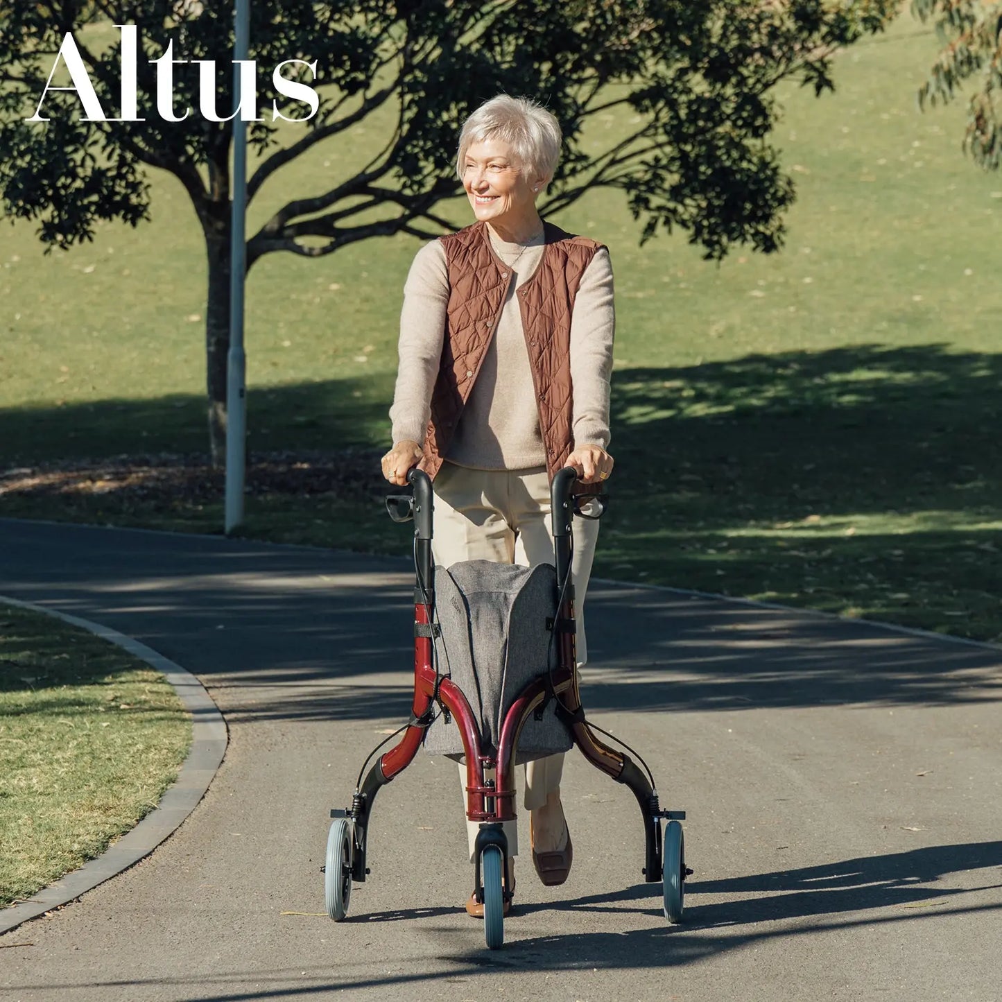 An elderly man using the Altus Rollator in an outdoor park setting. The image showcases the rollator’s stability and ease of use, allowing users to maintain an active lifestyle. The large wheels and comfortable handles are visible, emphasizing the rollator’s ergonomic design.