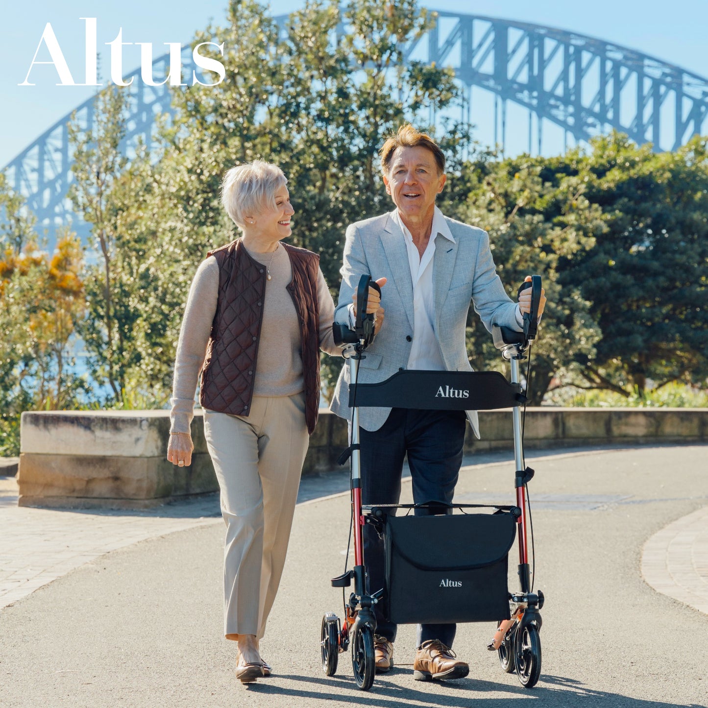 Two people walking with a walker in an outdoor setting with a bridge in the background