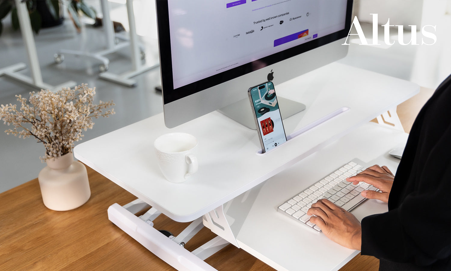 Side view of a height-adjustable desk riser with sturdy frame and large workspace, in a creative office setting.