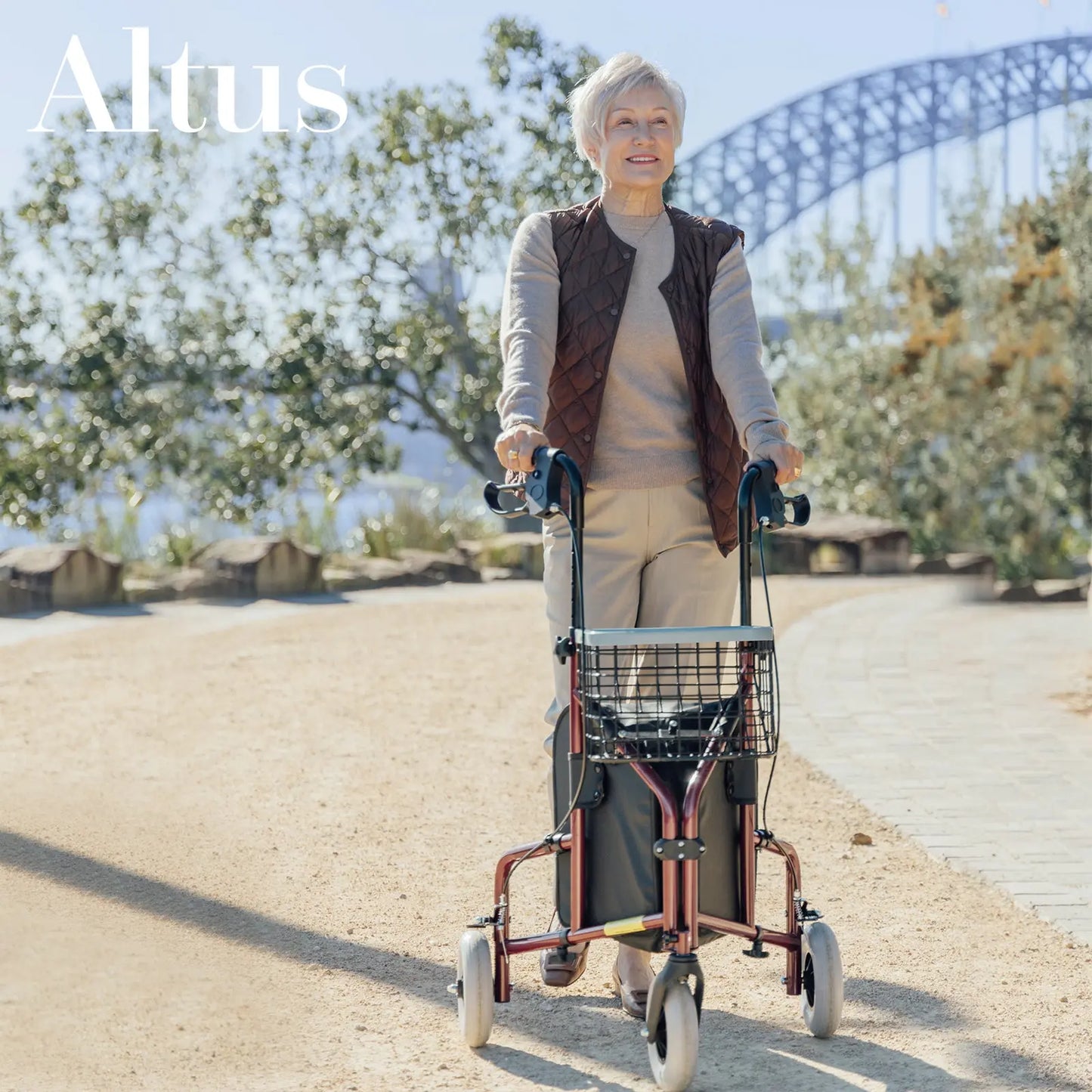 A senior woman walking with the Altus Rolling Walker Mobility Aid Rollator in Burgundy Red. This three-wheel rollator features a sturdy frame, ergonomic handles, and a convenient wire basket and tray, ideal for carrying personal items during outdoor activities.