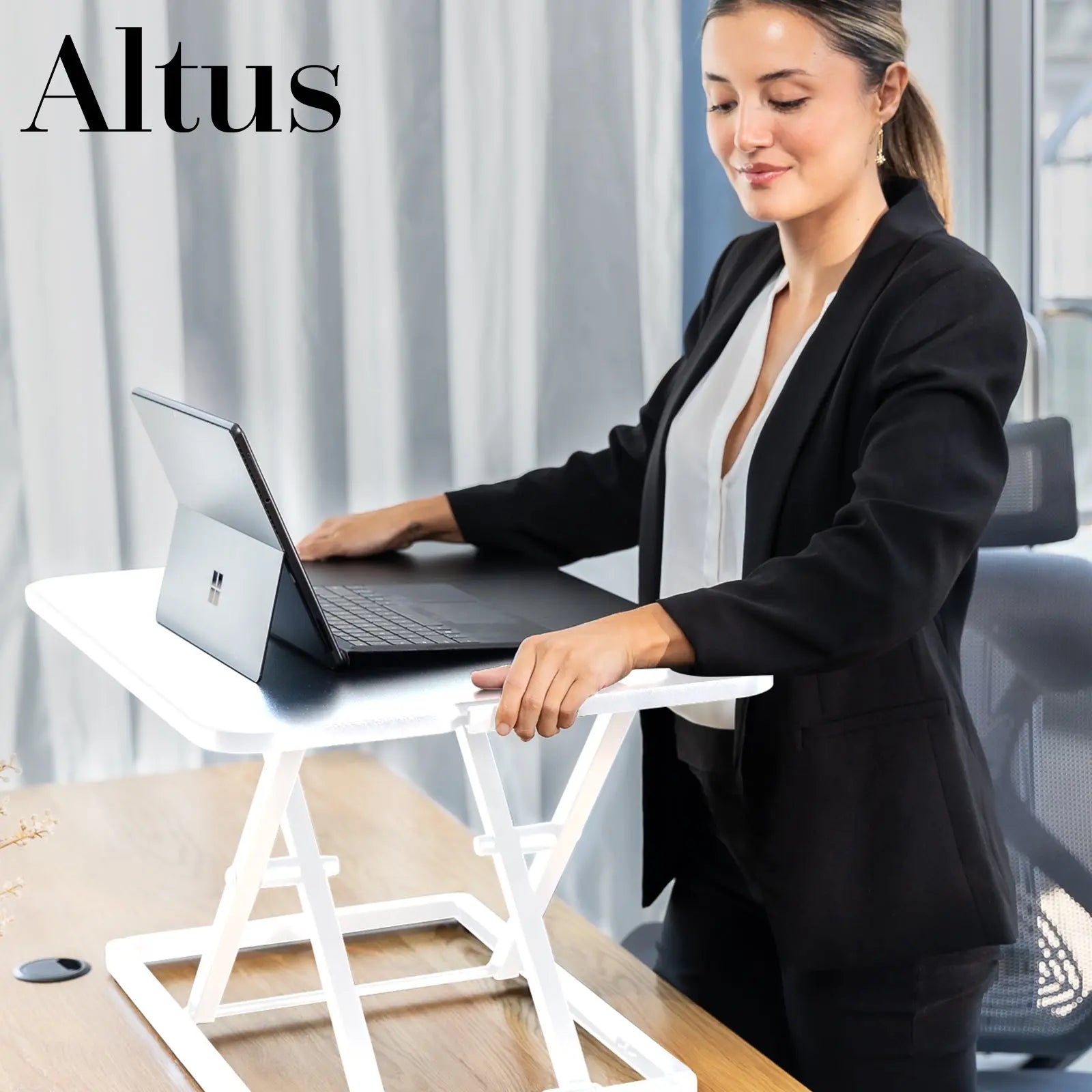 A professional woman in a business suit uses a white standing desk in an office environment, engaging with a laptop.