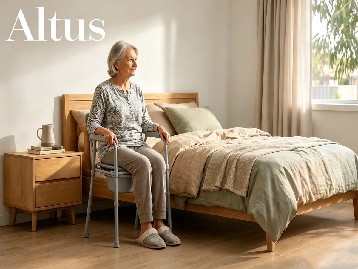An elderly woman sits on a gray Altus toilet training chair with a grab handle in a softly lit bedroom. The scene includes a wooden bed frame, beige bedding, a matching nightstand, and the brand name 'Altus' in white text at the top left.