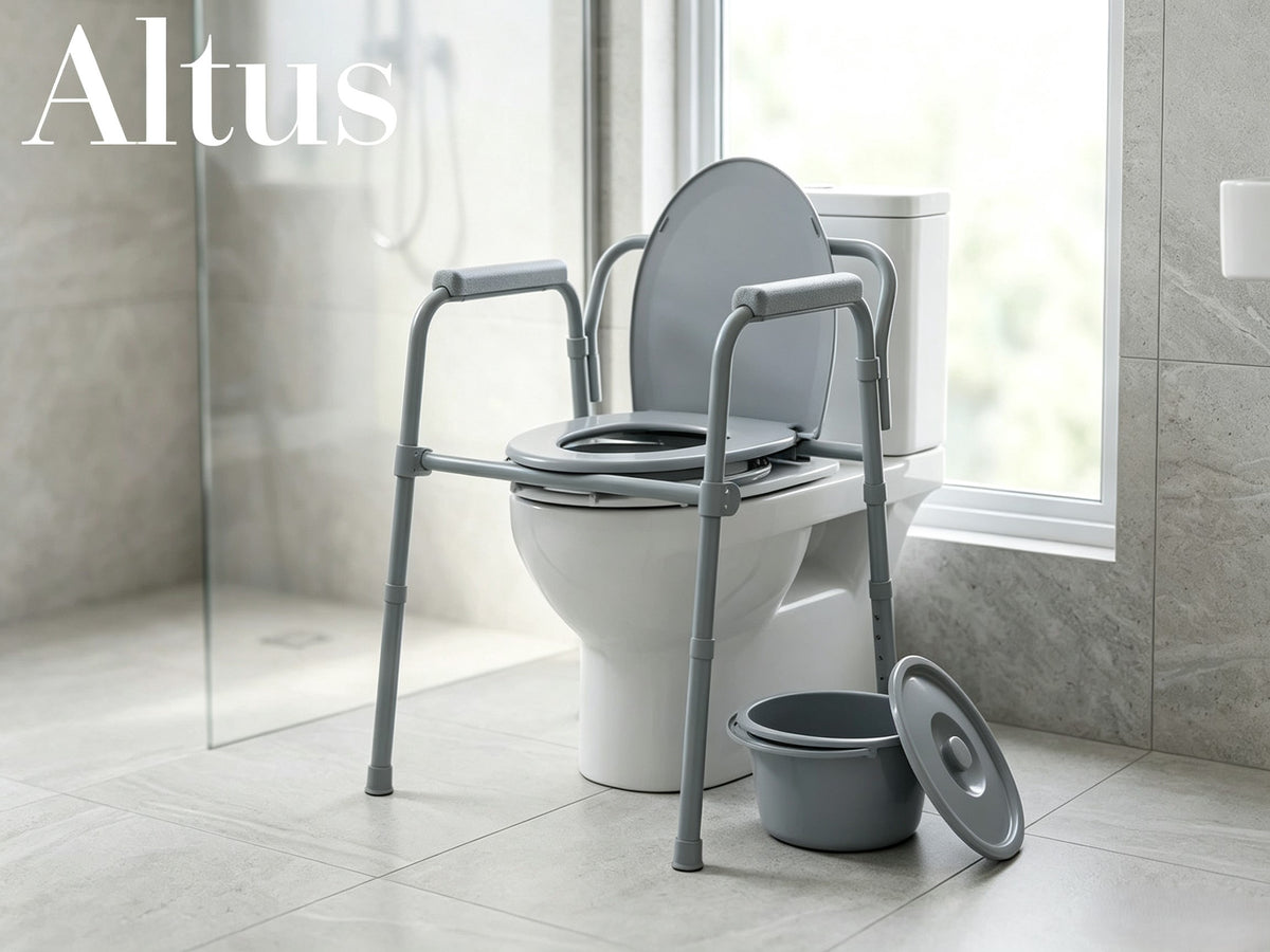 A gray plastic and metal portable toilet seat lift with armrests, shown installed on a white toilet in a modern tiled bathroom. A matching gray bucket and lid are placed on the floor beside it.
