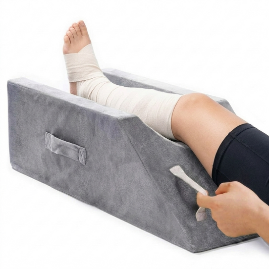 A gray wedge-shaped leg rest cushion with a handle, shown with a person's leg resting inside it on a white background.