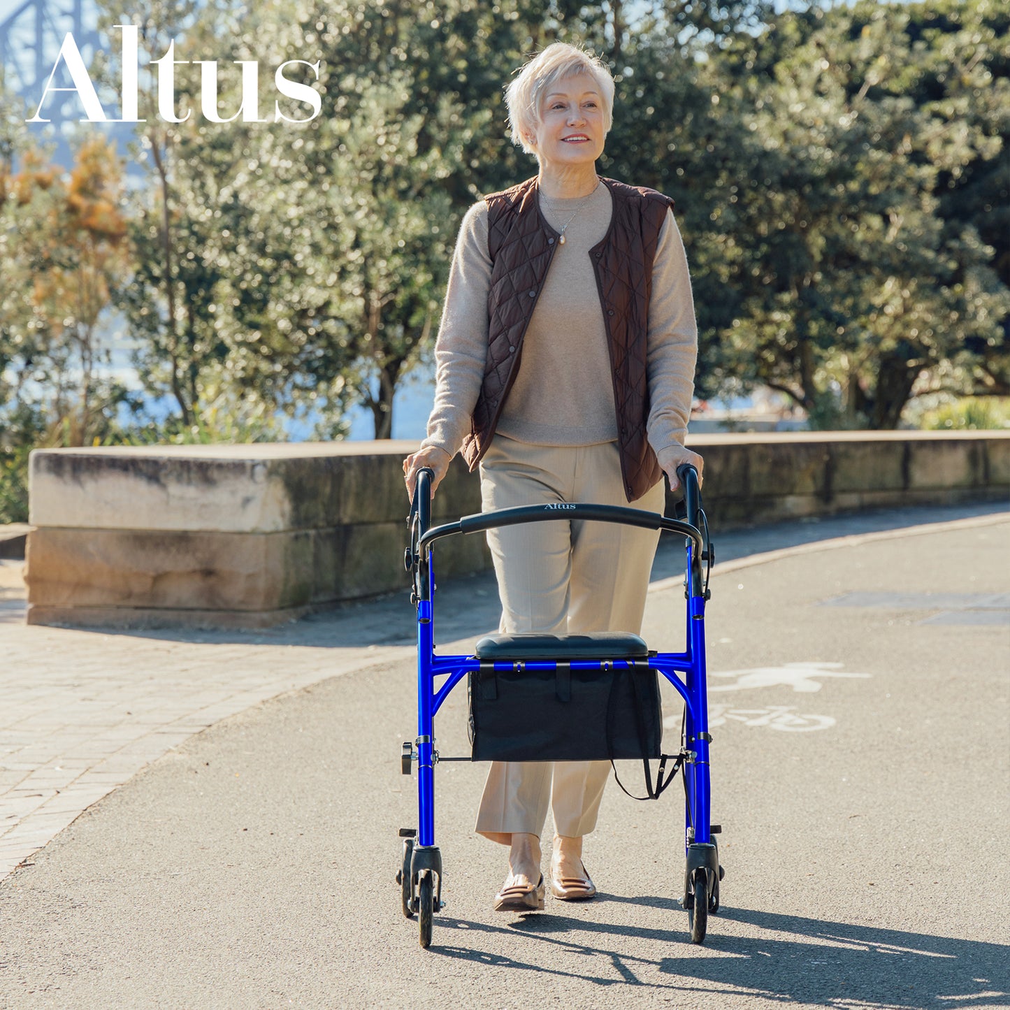 Woman using a blue walker outdoors with trees and a clear sky in the background