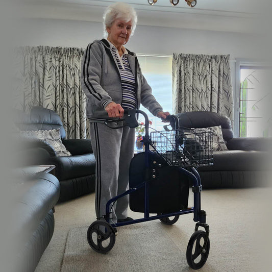 Senior woman using a walker in a living room with black leather couches and patterned curtains.