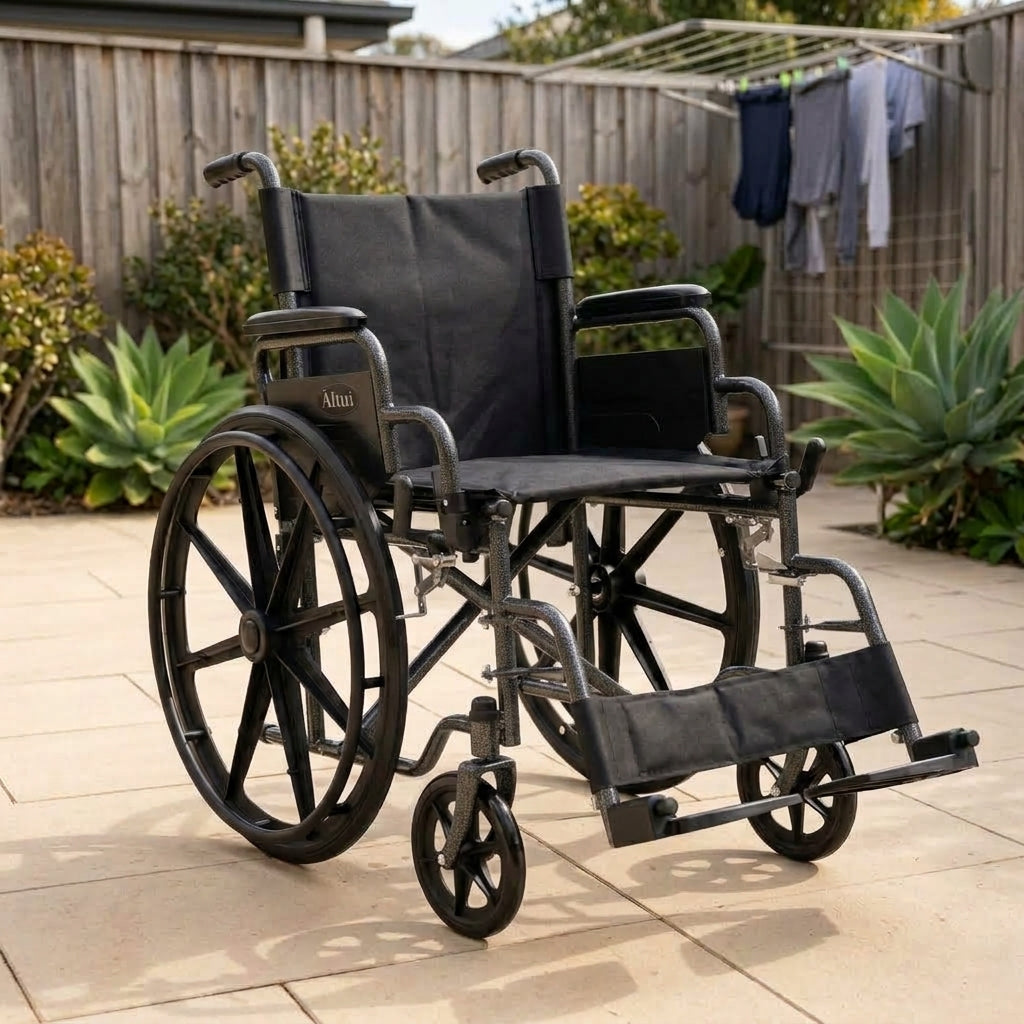 A black manual wheelchair with a padded seat and backrest, shown outdoors on a paved patio in a backyard setting with a wooden fence, plants, and a clothesline in the background.