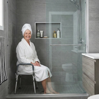 Woman in a white robe sitting in a shower with gray tiled walls and a glass door.