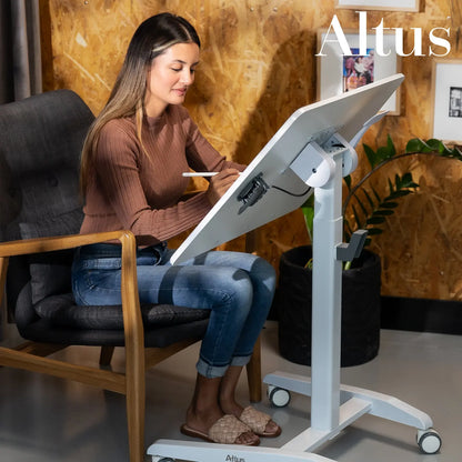 A focused woman works on a mobile desk with a tilted surface, ideal for reading or digital drawing, in an artistic home office setting.