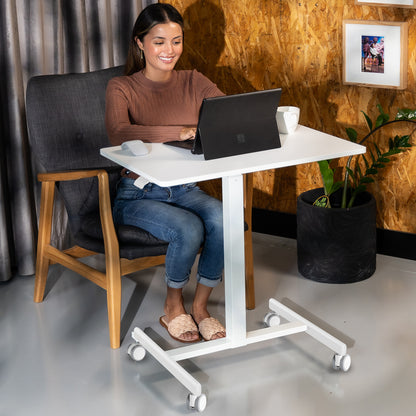 Woman using a laptop on a white adjustable desk in a home office setting.