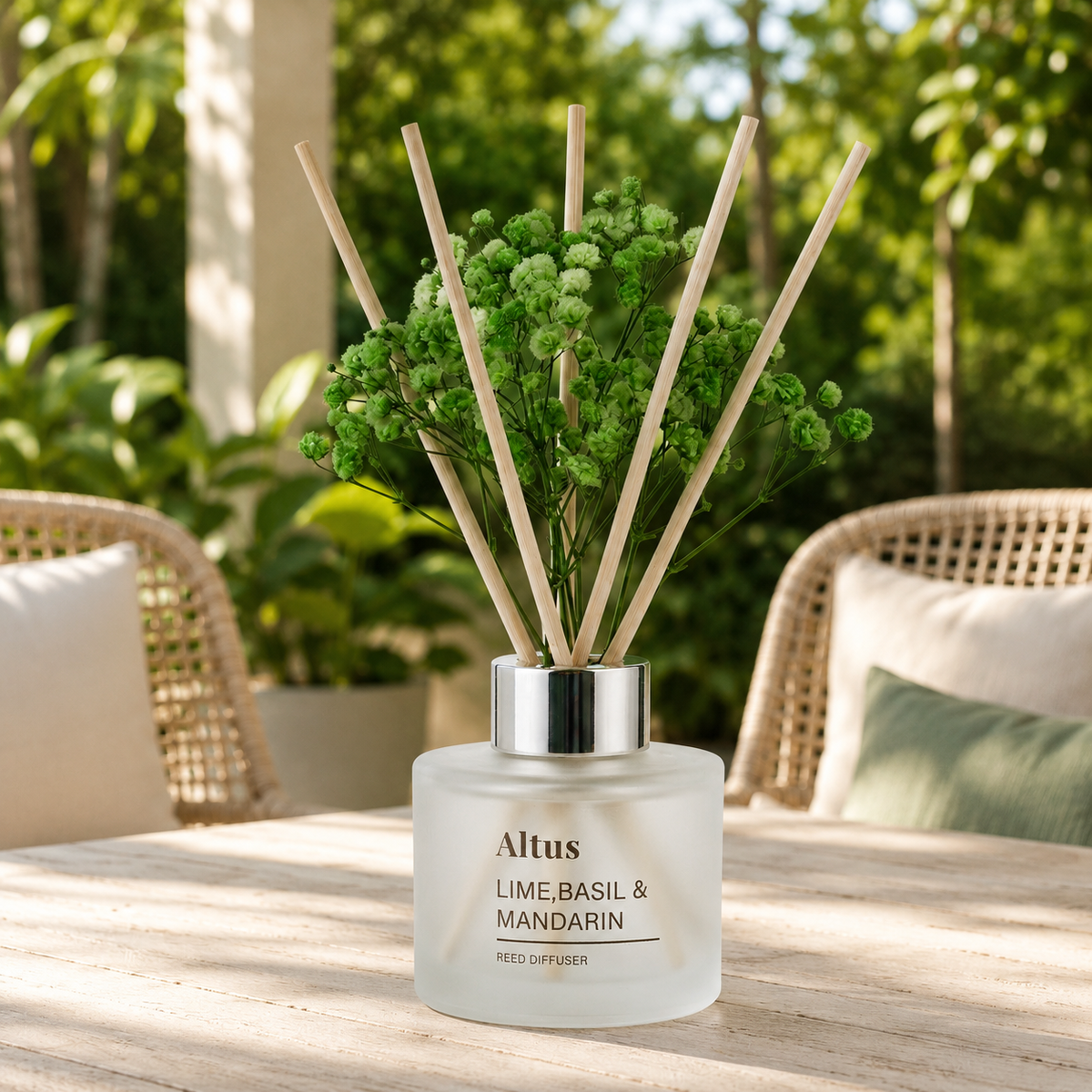 Altus Lime, Basil & Mandarin reed diffuser bottle with natural wood reeds and green dried flowers, displayed on a wooden table in a garden patio setting.