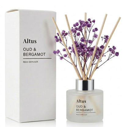 Altus Oud & Bergamot reed diffuser with a frosted glass bottle, purple dried flowers, and natural reed sticks, shown next to its white cardboard packaging box on a white background.