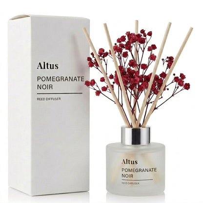 Altus Pomegranate Noir reed diffuser with a frosted glass bottle, natural wooden reeds, and dried red pomegranate blossoms, shown next to its white packaging box.
