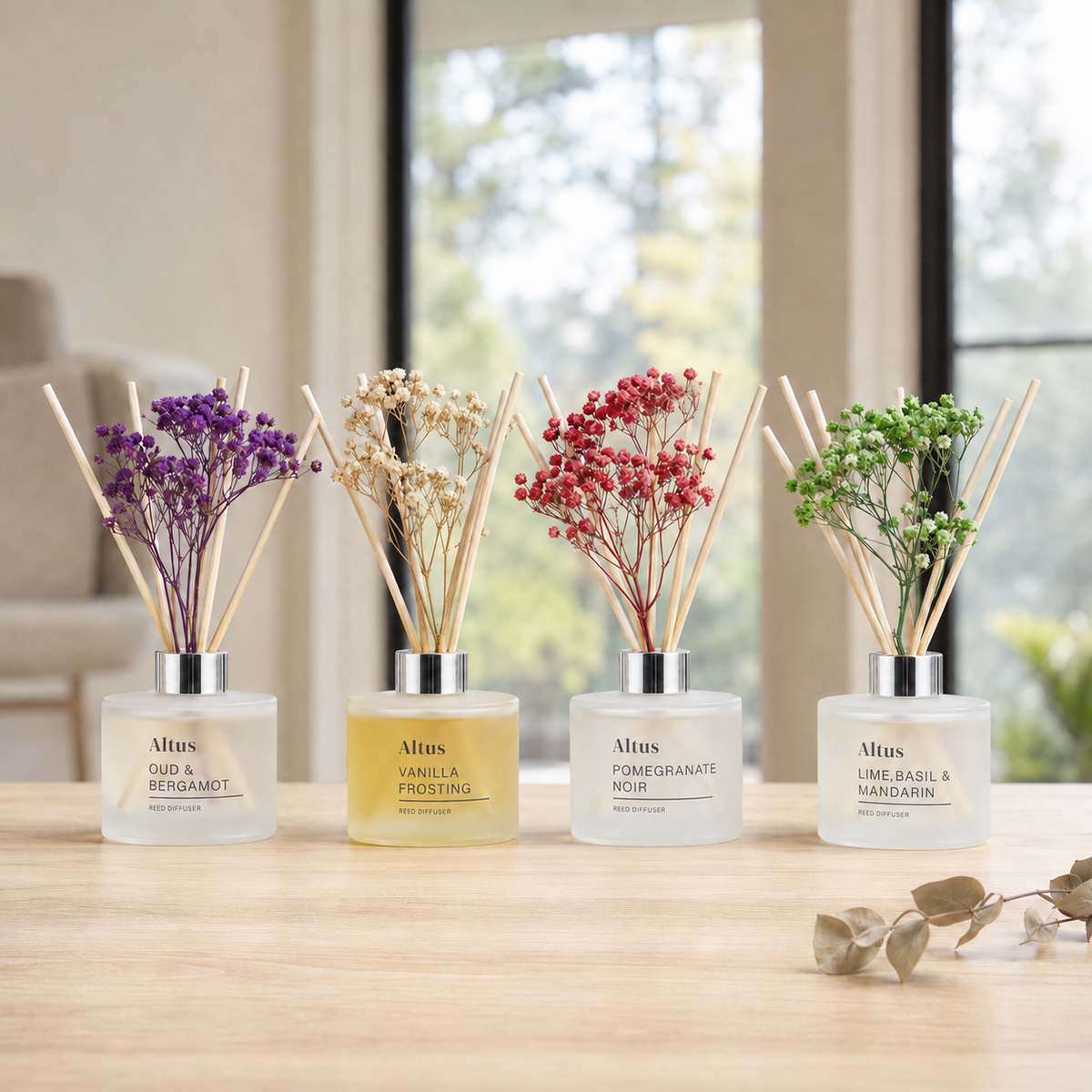 Four AltUS reed diffusers with dried flowers in frosted glass bottles, arranged on a light wood table in a softly blurred indoor setting.