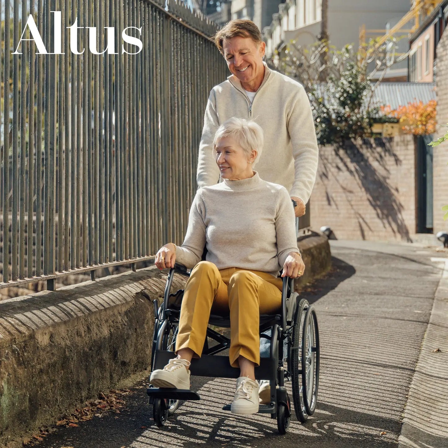 A senior couple enjoying a walk with the Altus 20-Inch Wheelchair in Black. The wheelchair's lightweight design and smooth-rolling wheels ensure ease of use and maneuverability, making it perfect for both indoor and outdoor activities.