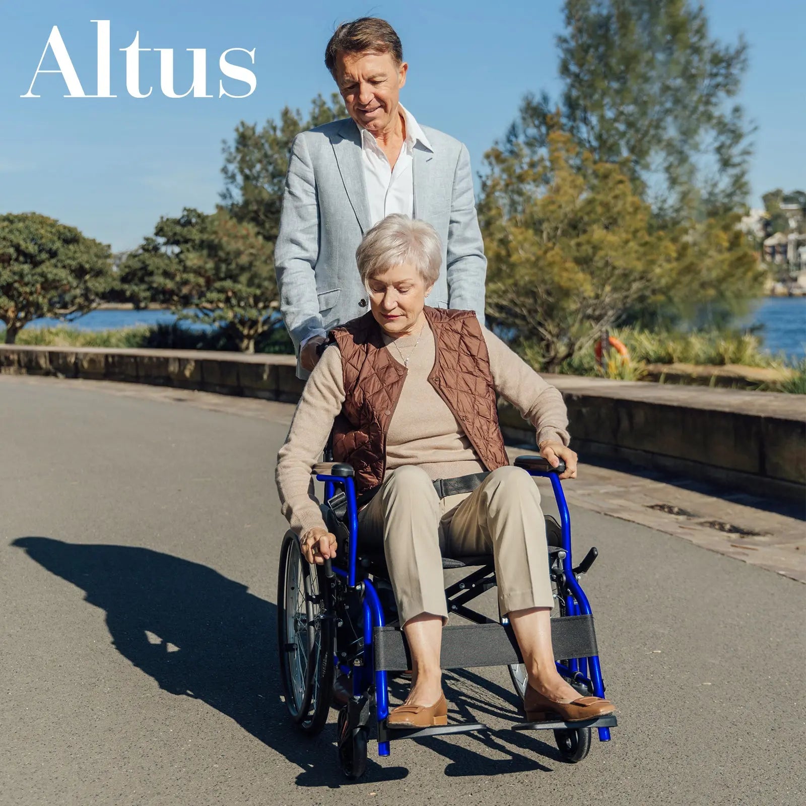 A senior couple enjoying a walk with the Altus 20-Inch Wheelchair in Blue. The wheelchair's lightweight design and smooth-rolling wheels ensure ease of use and maneuverability, making it perfect for both indoor and outdoor activities.