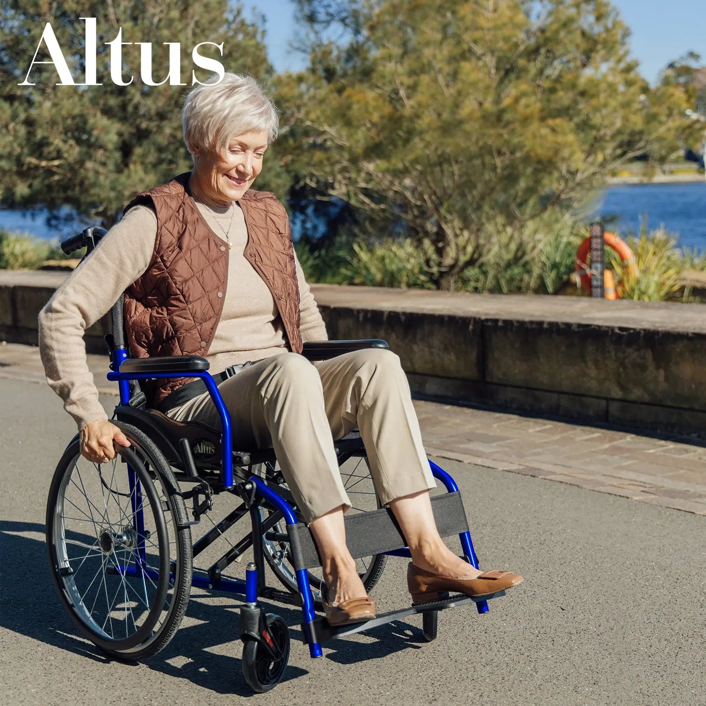 A senior woman sitting comfortably in the Altus 20-Inch Wheelchair in Blue. This wheelchair features a durable frame, ergonomic design, and easy-to-use footrests, providing excellent support and mobility for users.