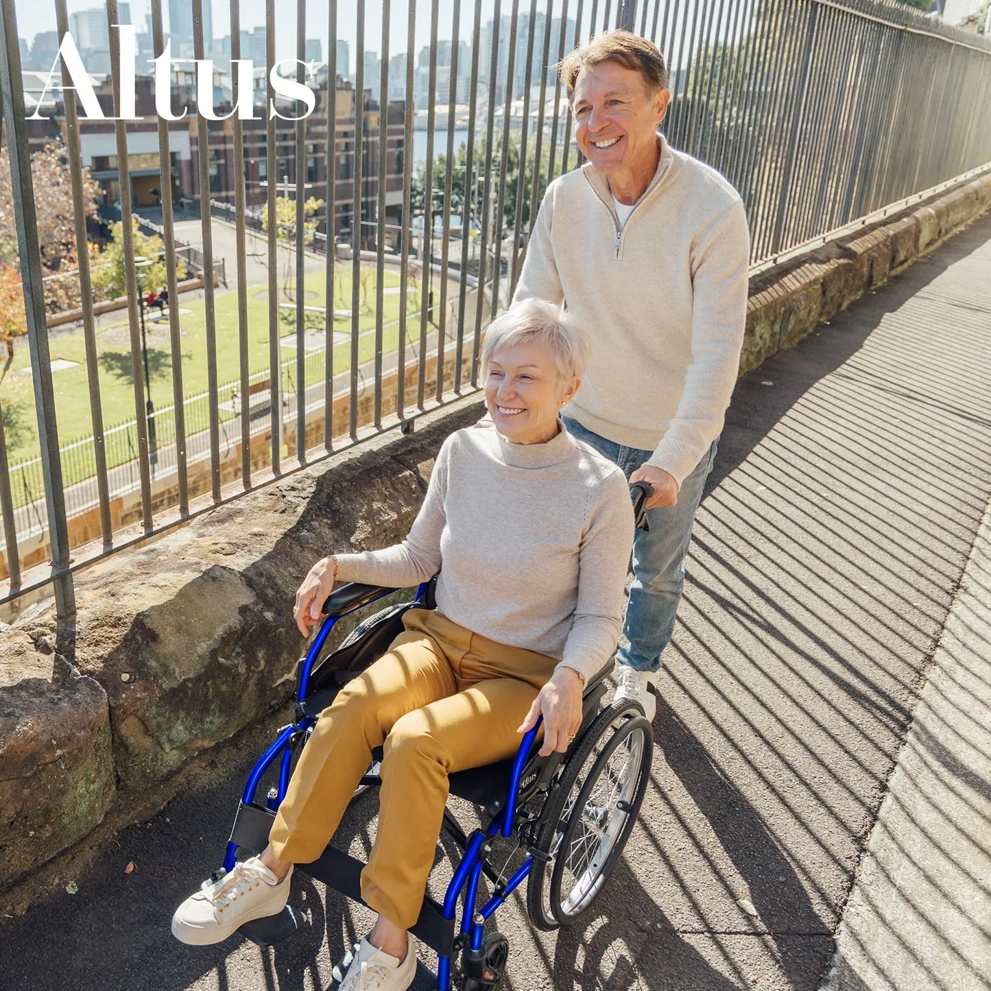 A senior couple enjoying a walk with the Altus 20-Inch Wheelchair in Blue. The wheelchair's lightweight design and smooth-rolling wheels ensure ease of use and maneuverability, making it perfect for both indoor and outdoor activities.