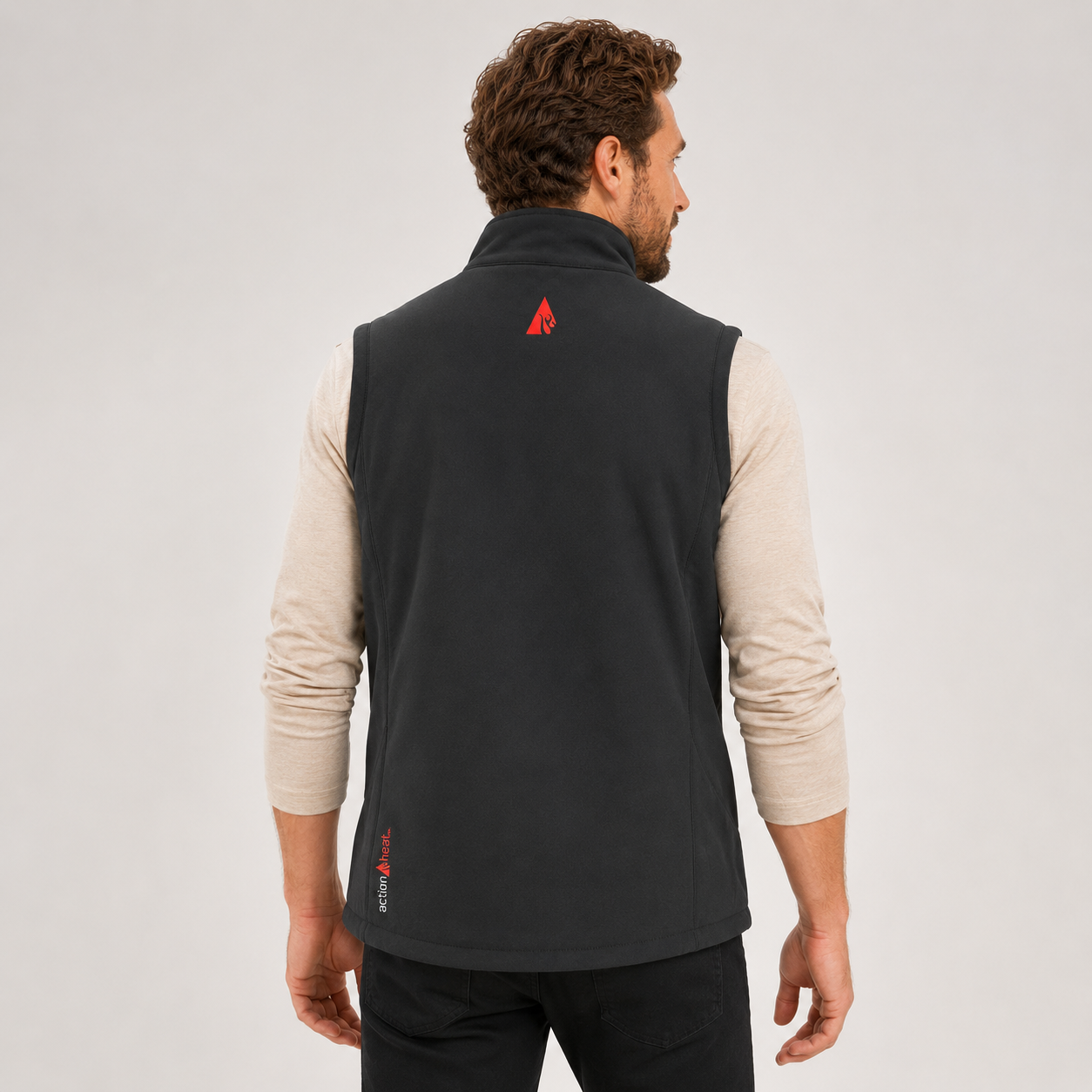 Man wearing a black vest with a red logo on the back against a light gray background