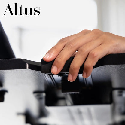 The Altus desk riser shown from a side angle in an office setting, with a laptop, coffee cup, and mobile phone placed on its surface.