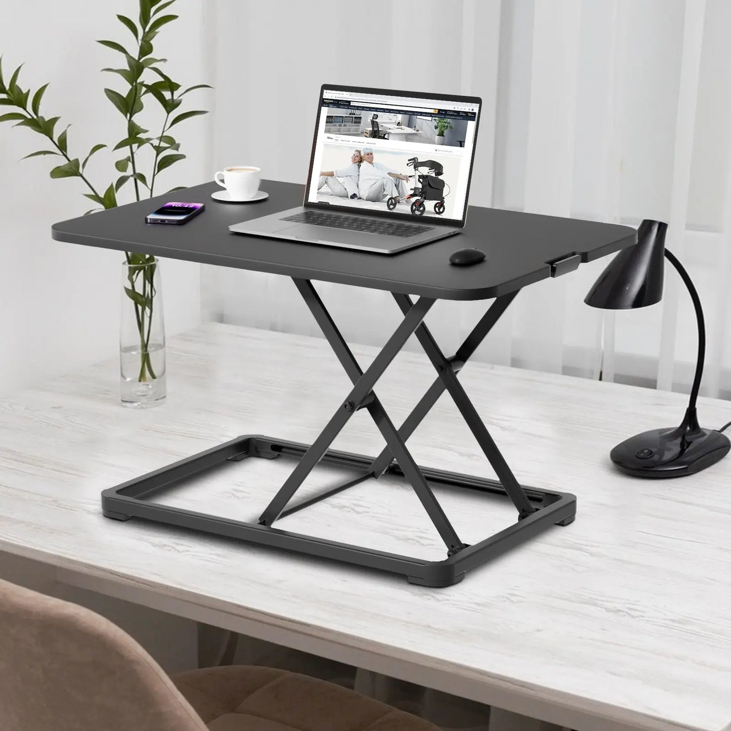 The Altus desk riser shown from a side angle in an office setting, with a laptop, coffee cup, and mobile phone placed on its surface.