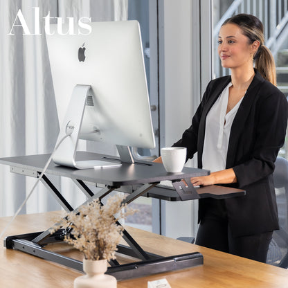 Woman using a standing desk with a computer setup, featuring the brand 'Altus'.