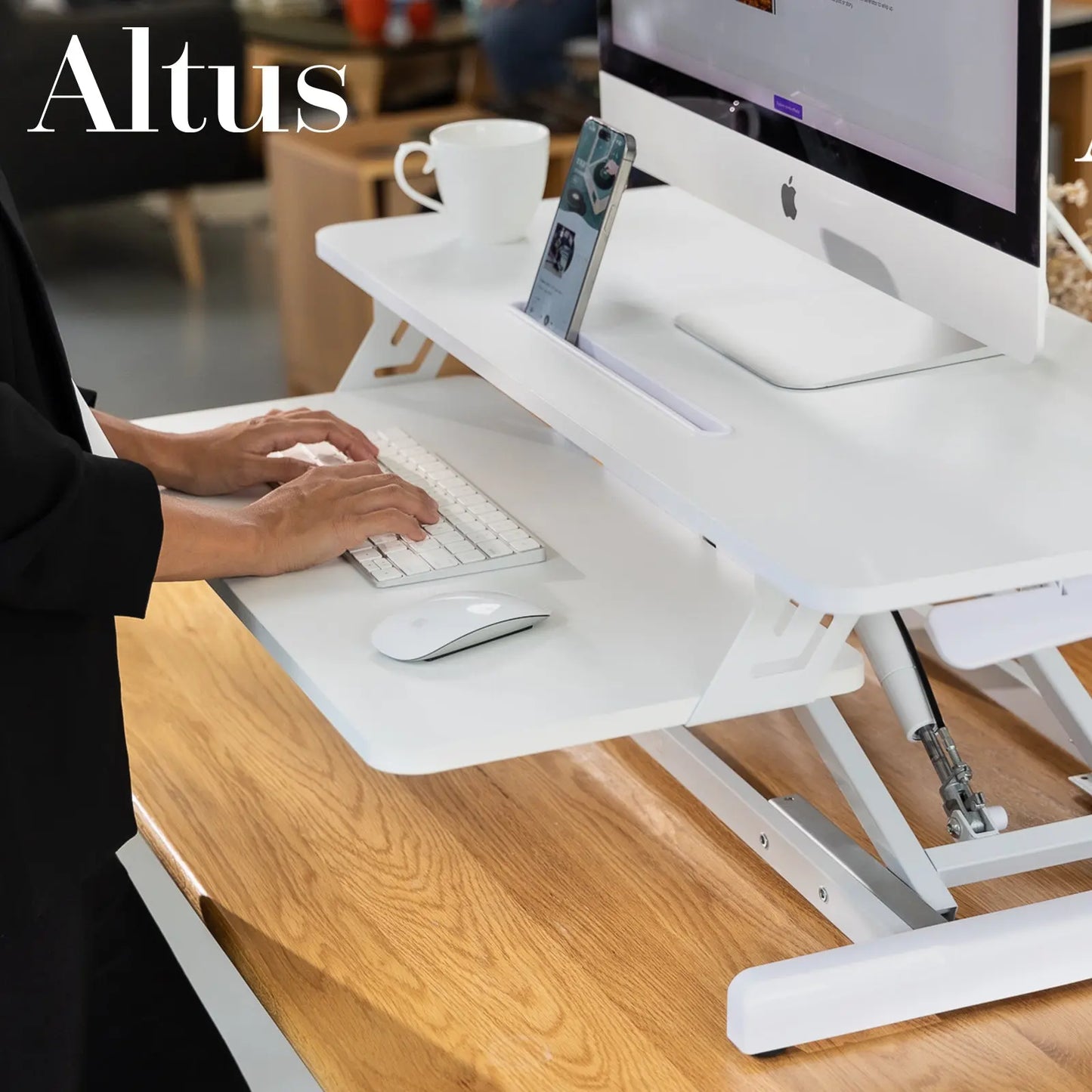 Side view of a height-adjustable desk riser with sturdy frame and large workspace, in a creative office setting.