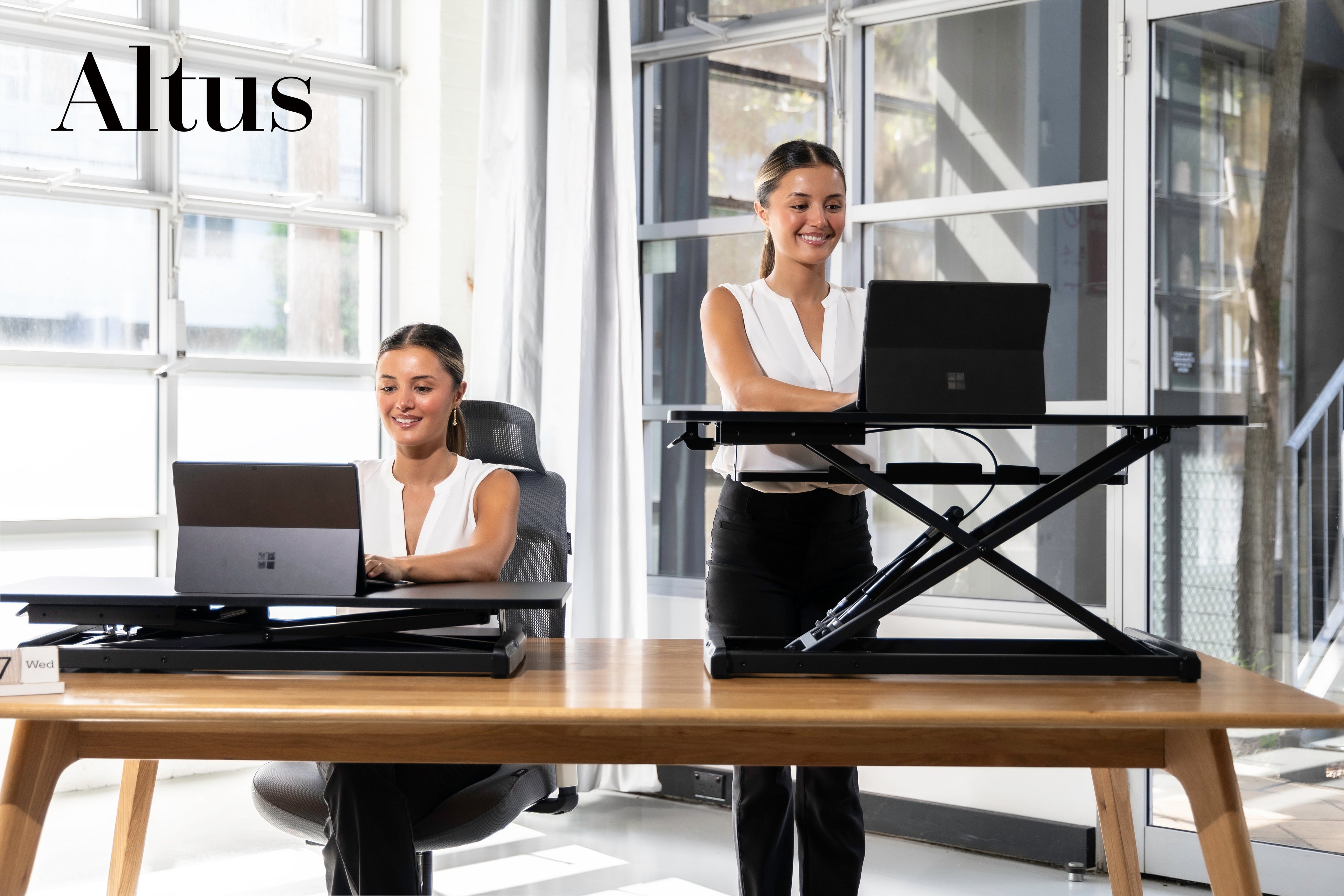 Woman standing at modern ergonomic sit-stand desk riser with the  monitors for healthy workspace setup.