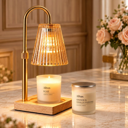 Altus home fragrance collection featuring a brass table lamp with a ribbed glass shade and a wooden base, alongside two scented candles in glass jars and their white packaging boxes. The candles are labeled 'Altus ROSE' and 'Altus ORANGE & VANILLA PUDDING'.