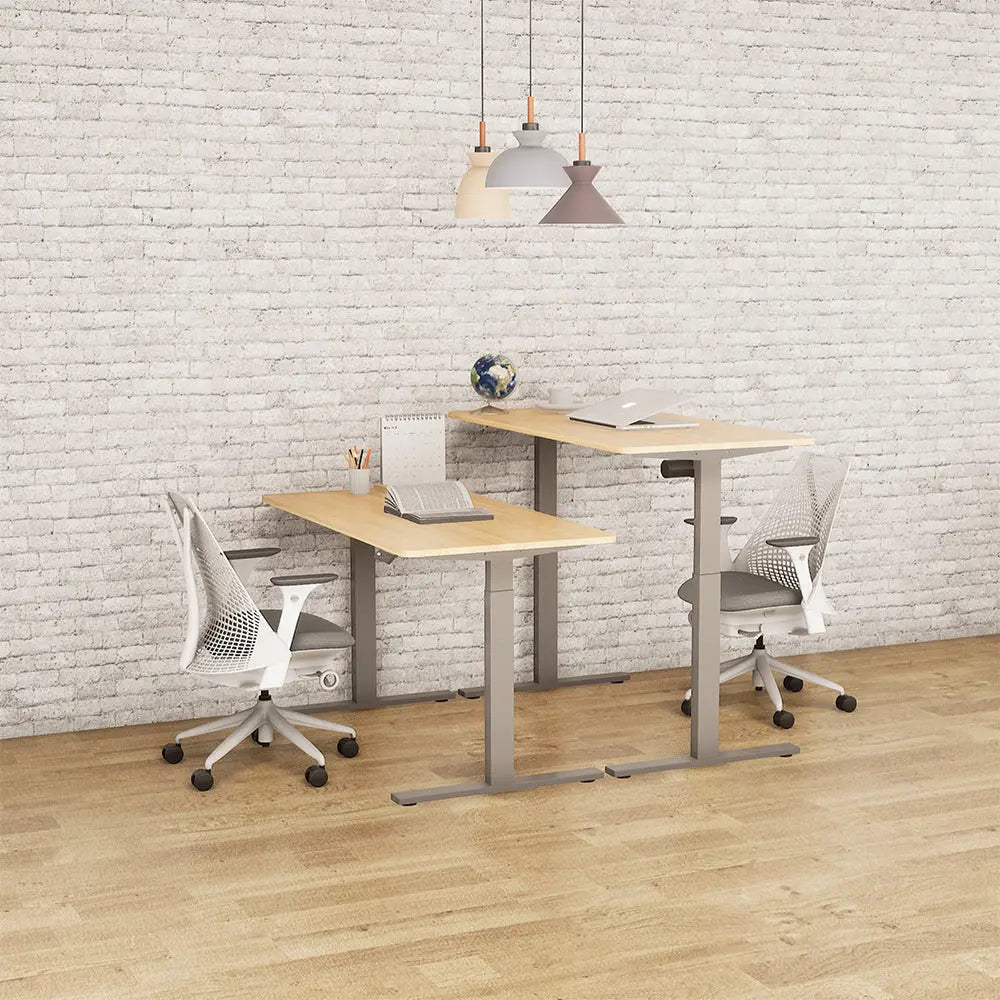 A stylized office scene with two motorized adjustable desks set in a brick-walled room, demonstrating a collaborative and modern workspace environment.